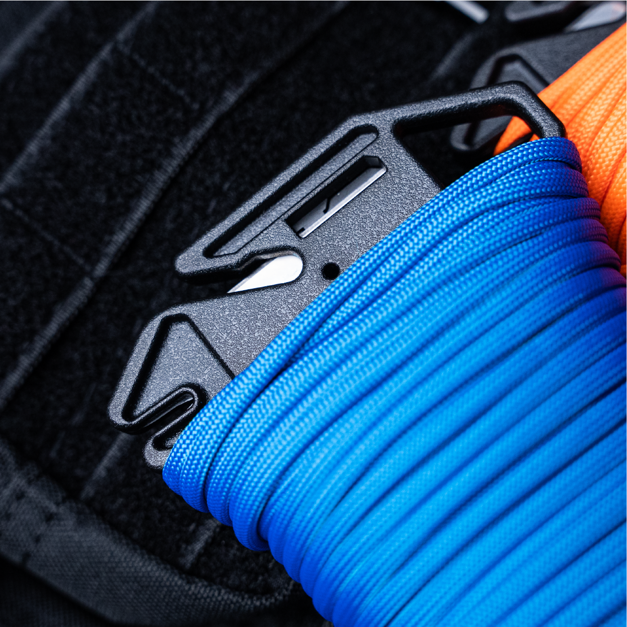 Closeup of Ready Rope's built in cutting blade and gear loop. 100ft of Blue Paracord pre loaded, lying on backpack